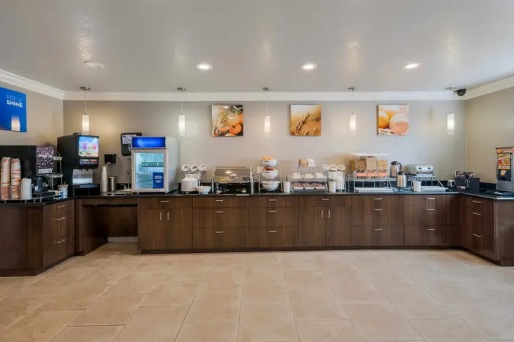 Breakfast room with a long buffet counter, coffee and juice machines, a waffle station and bright food photos on the wall