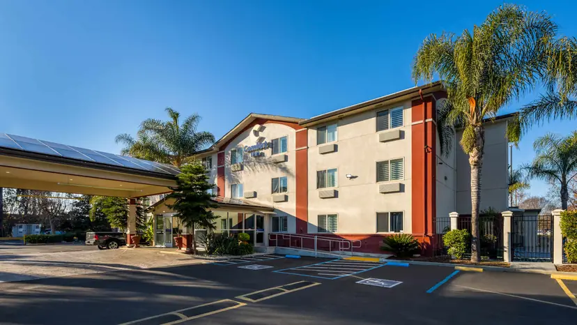 Comfort Inn Gilroy: a three-story cream and red building with a Comfort Inn sign, tall palm trees and a covered entrance under a blue sky